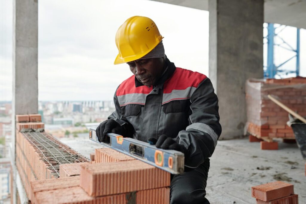mature builder in workwear and protective helmet using level handtool